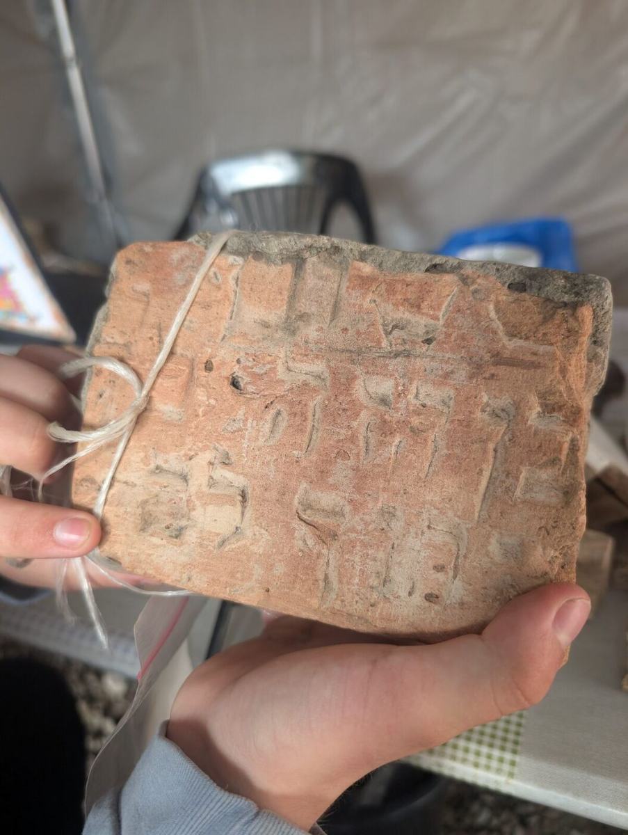 A broken matzevah fragment with carved Hebrew letters held in two hands