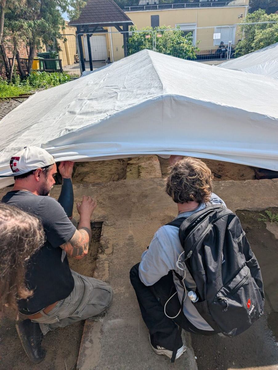 Two people lifting a tarp over an excavated area in the cemetery