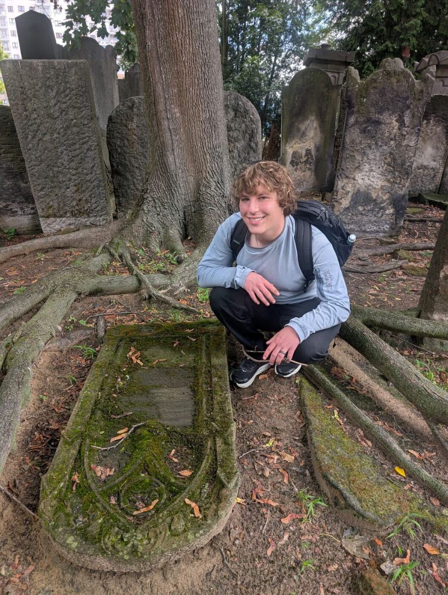 Jules crouched beside a fallen matzevah at the Warsaw Jewish Cemetery