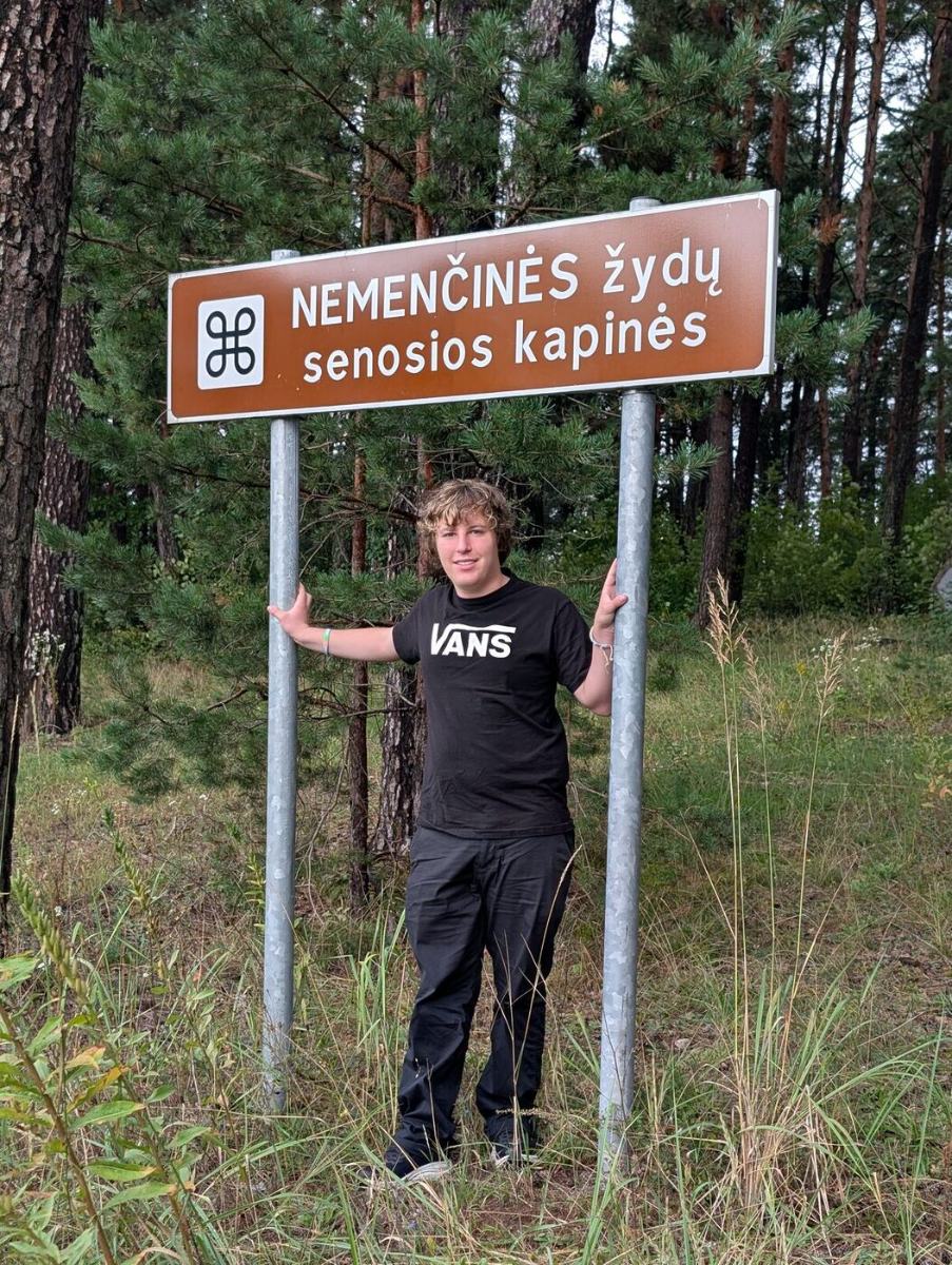 Jules beneath the sign reading Nemenčinės žydų senosios kapinės